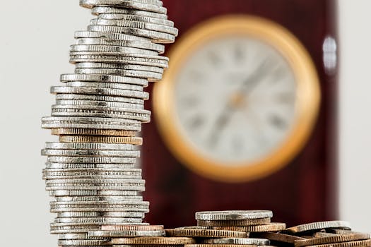 A close-up image of stacked coins with a blurred clock, symbolizing time and money relationship.